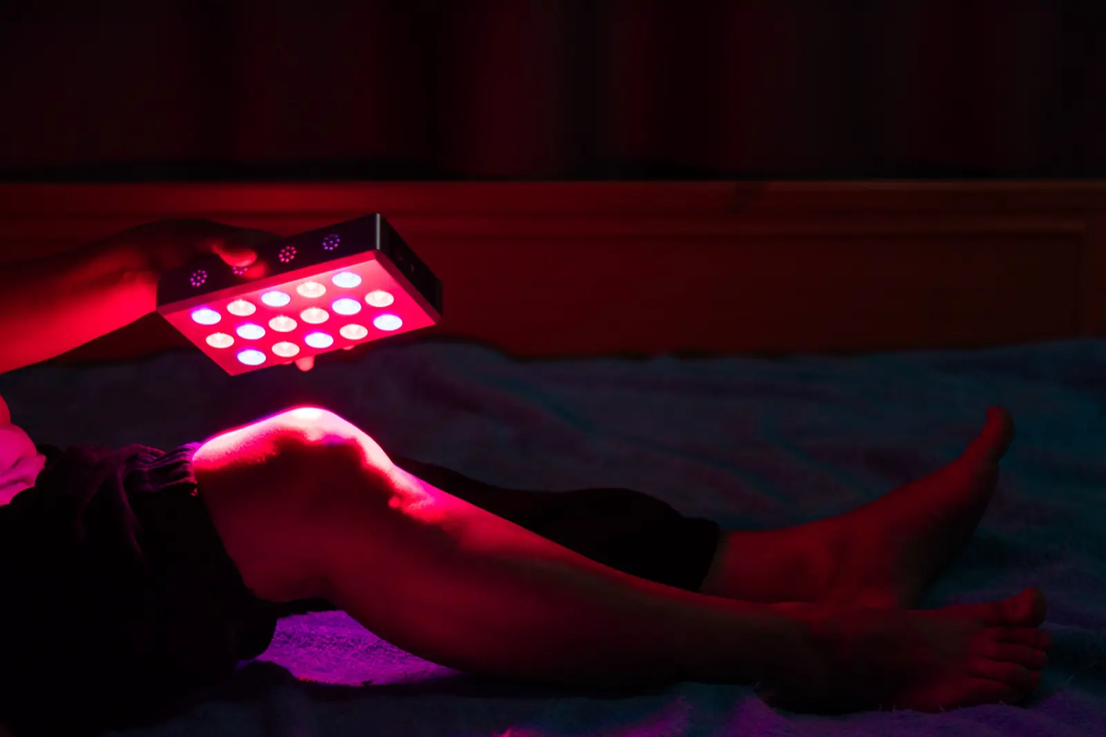 Closeup of treating sore leg with the red light therapy handheld device at home on the bed