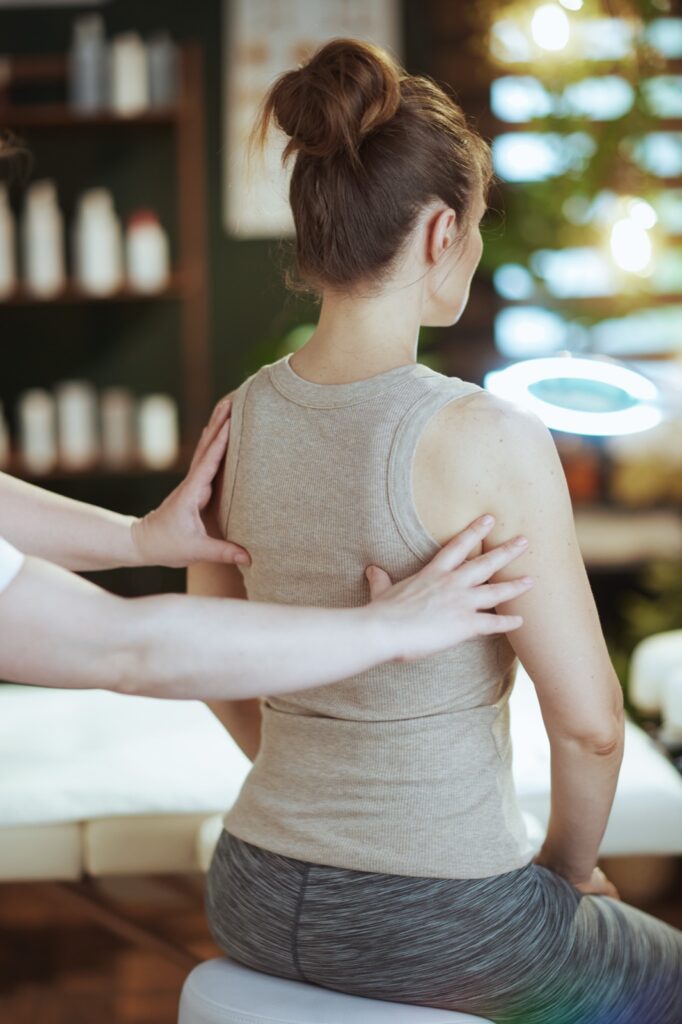 Healthcare time. Seen from behind medical massage therapist in spa salon checking clients back condition during examination.